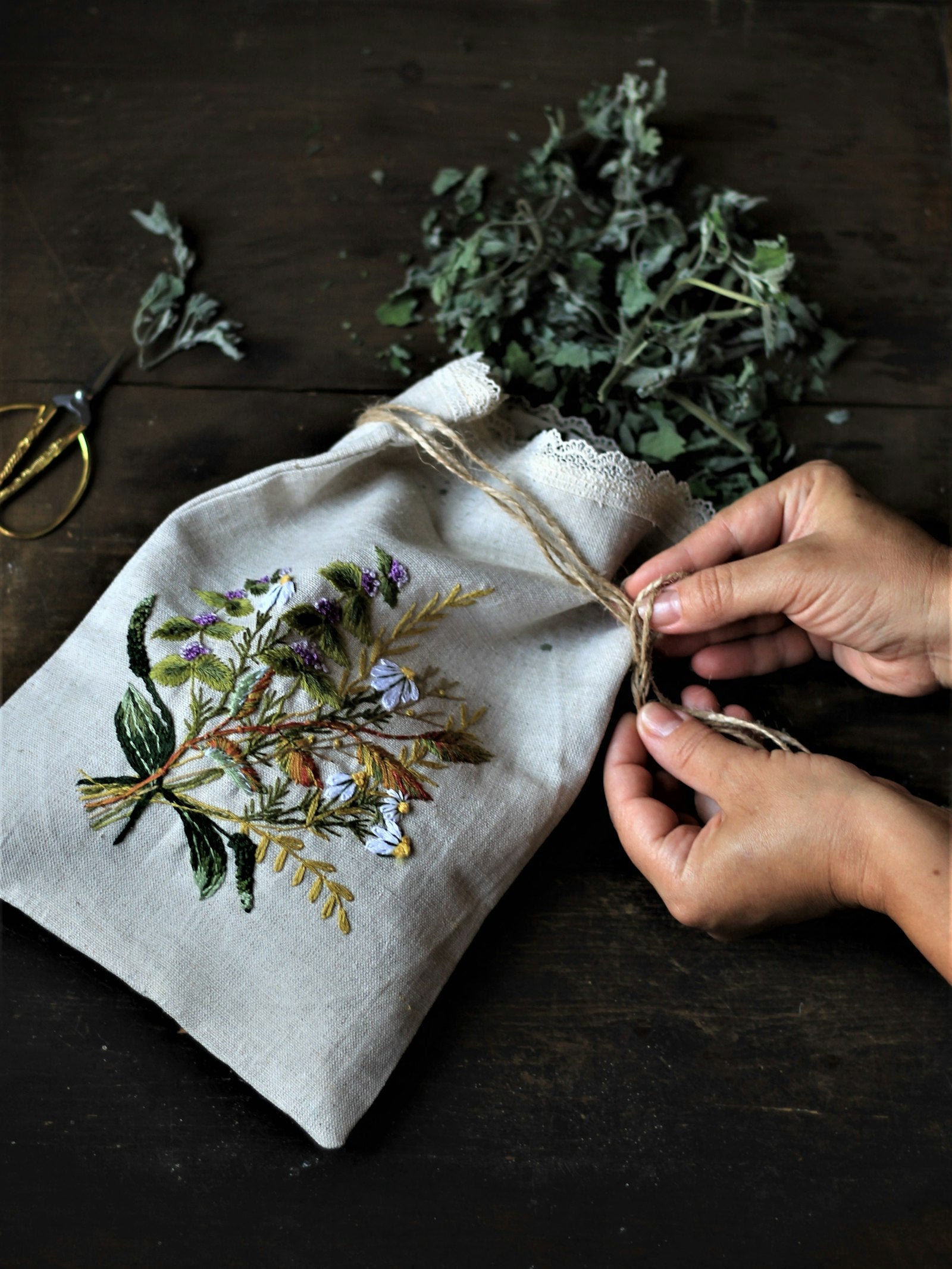 Hands tying the jute cord of a hand embroidered linen bag